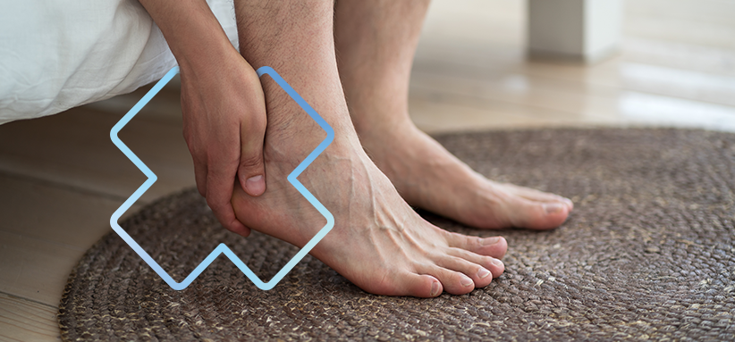 Personne assise au bord d’un lit tenant son talon avec la main, illustrant une douleur au talon ou à la cheville, avec un symbole graphique bleu superposé près de la zone douloureuse.