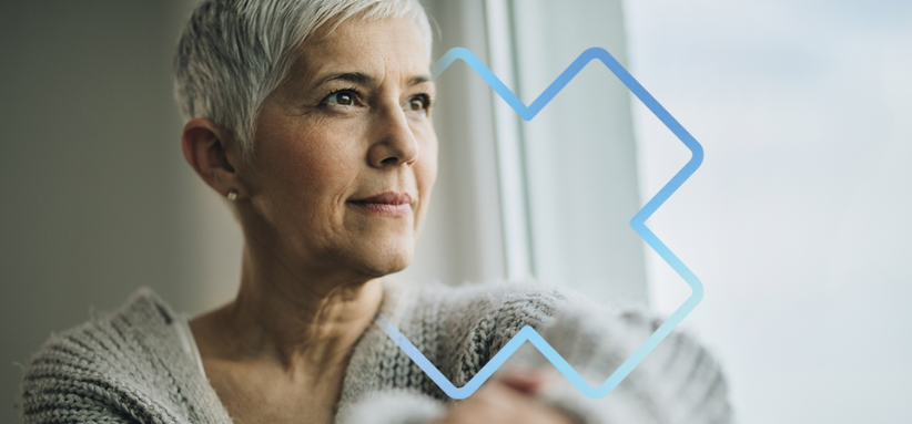Personne portant un chandail en tricot gris, les bras croisés, assise près d’une fenêtre laissant entrer une lumière naturelle. Un symbole graphique bleu en forme de croix médicale est superposé à l’image, évoquant les soins de santé, le soutien et le bien-être.