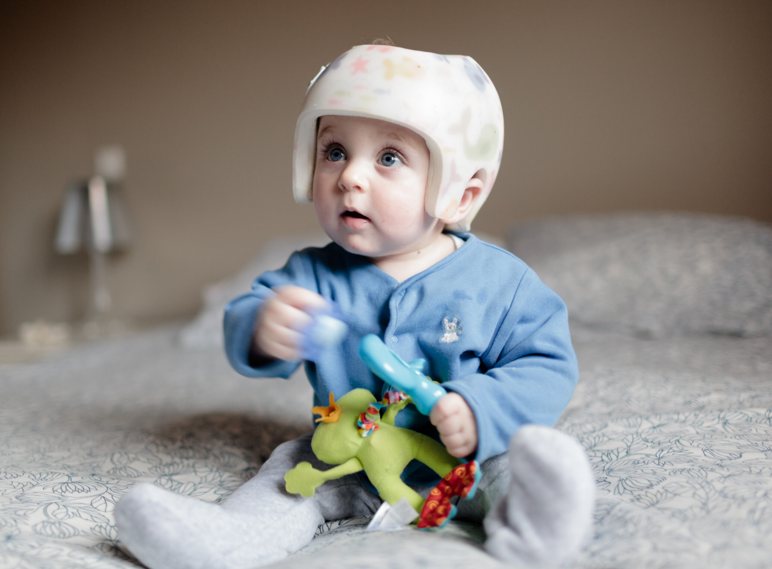 cute baby boy 6 months old looking at camera. He is wearing a helmet to correct plagiocephaly