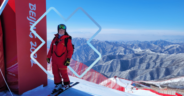 Skieuse debout au sommet d’une piste avec une vue sur les montagnes, illustrant la pratique du ski de haut niveau aux Jeux olympiques.
