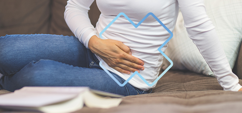 Personne assise tenant le bas de l’abdomen, illustrant une problématique traitée en rééducation périnéale et pelvienne.
