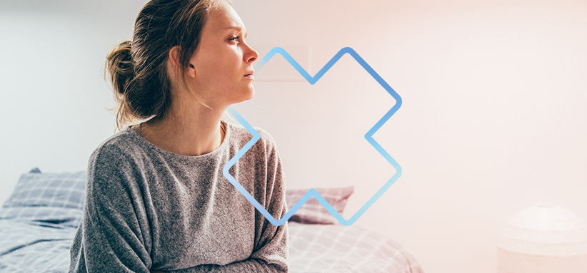 Personne assise sur un lit regardant vers la gauche, dans un environnement calme, avec un contour graphique bleu en forme de croix médicale en avant-plan.